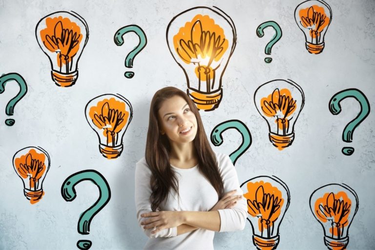 young lady standing in front of a wall filled with cartoon drawings of lightbulbs and question marks